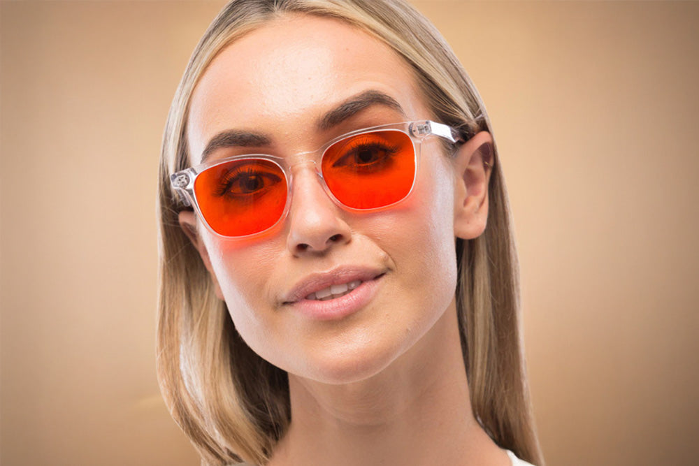 Woman wearing red-tinted, blue light blocking glasses. Against a beige, brown background.